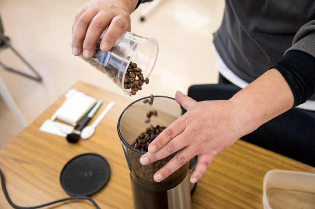 焙煎したコーヒー豆をグラインダーに入れているコーヒーづくりの作業風景